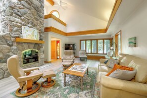 A spacious living room with a stone wall, a fireplace, leather furniture, and large windows.