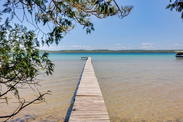 A wooden pier extending into a clear blue body of water, surrounded by trees.