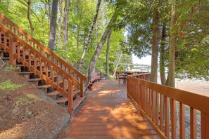 A wooden deck leading to a dock, surrounded by tall trees.