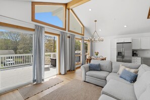 Un soggiorno spazioso con un ampio divano grigio, un'area pranzo con tavolo e sedie, una cucina dotata di elettrodomestici moderni e un balcone con ringhiera.