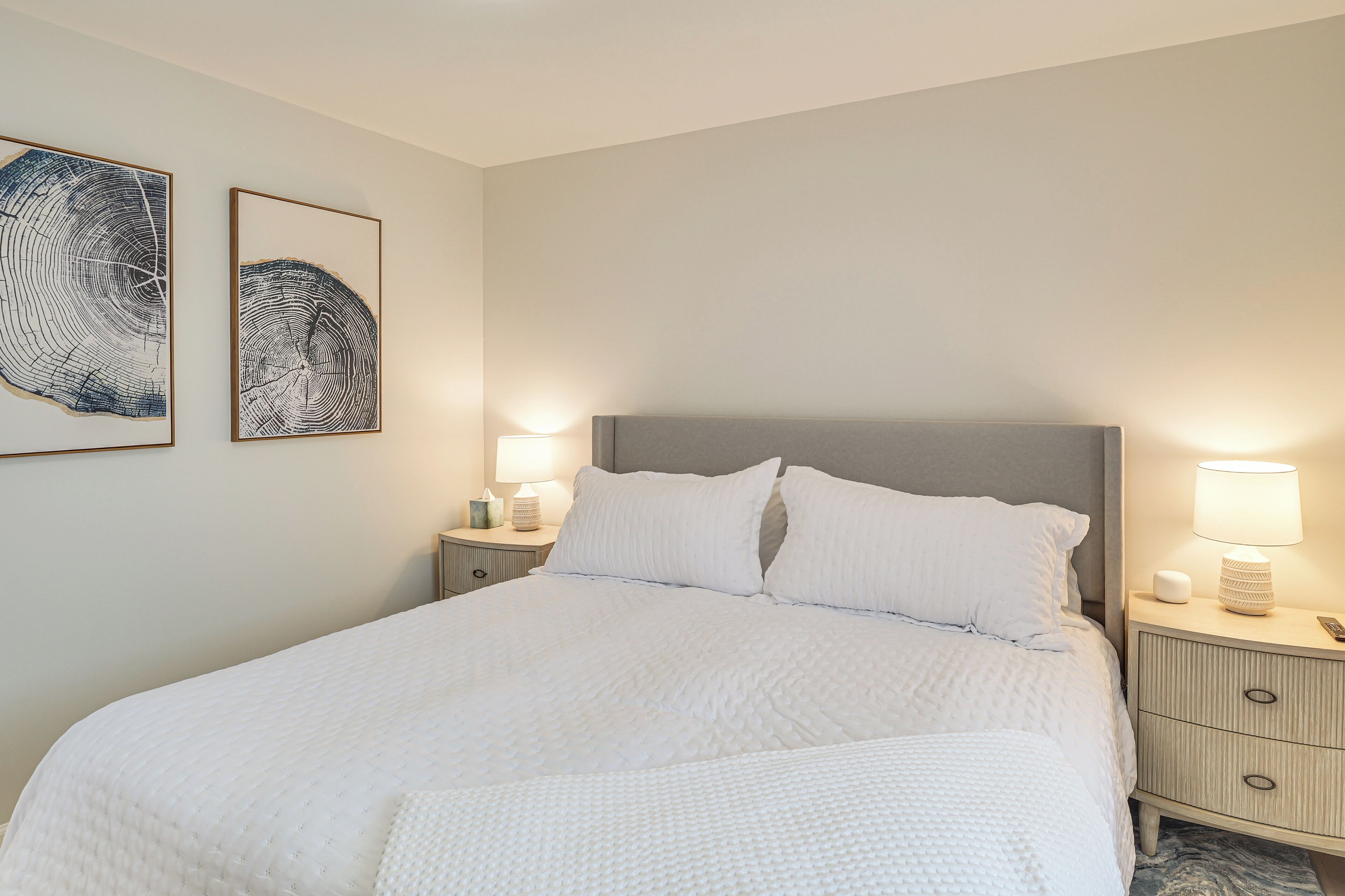 A neatly made bed with white bedding, a grey headboard, and two bedside lamps.