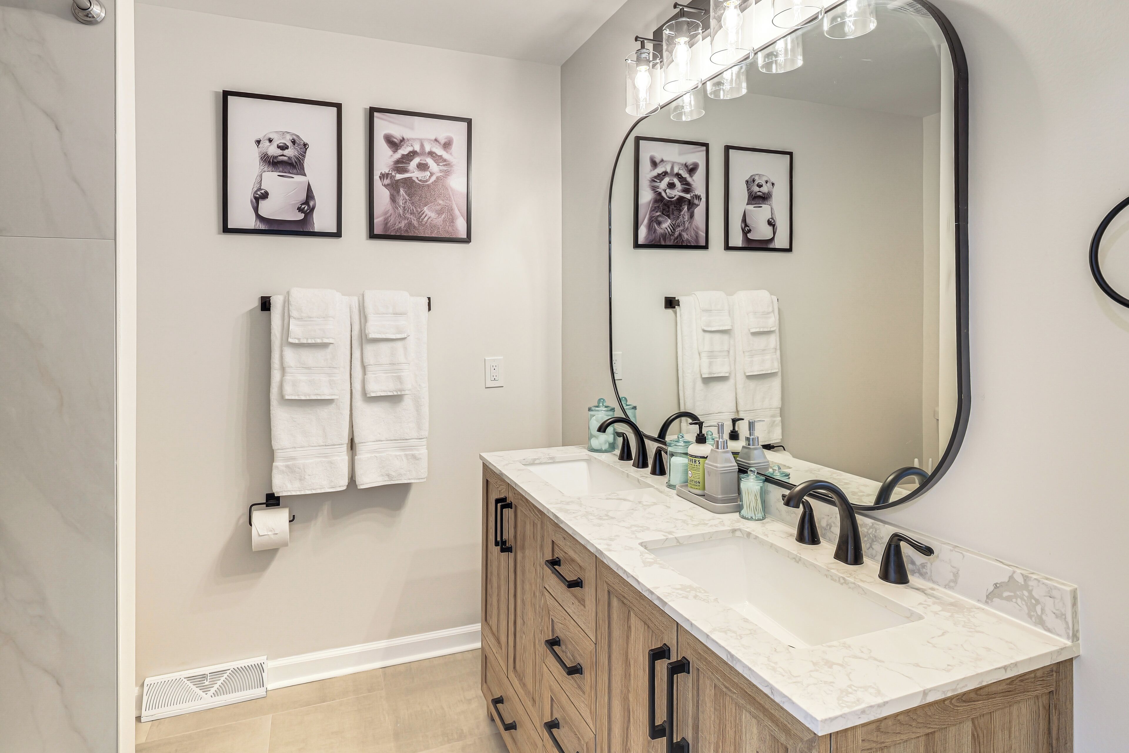 A bathroom with a large mirror, a sink, and two framed animal pictures on the wall.