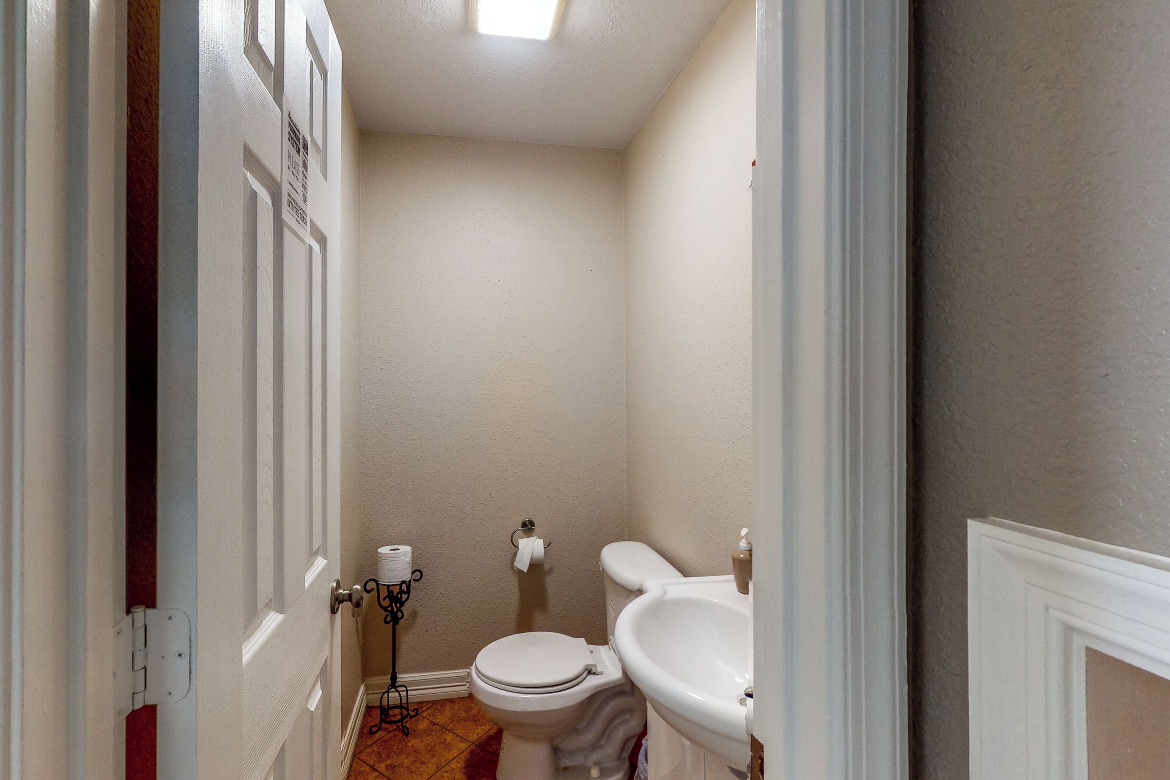 A small bathroom with a toilet, sink, and a roll of toilet paper on the floor.