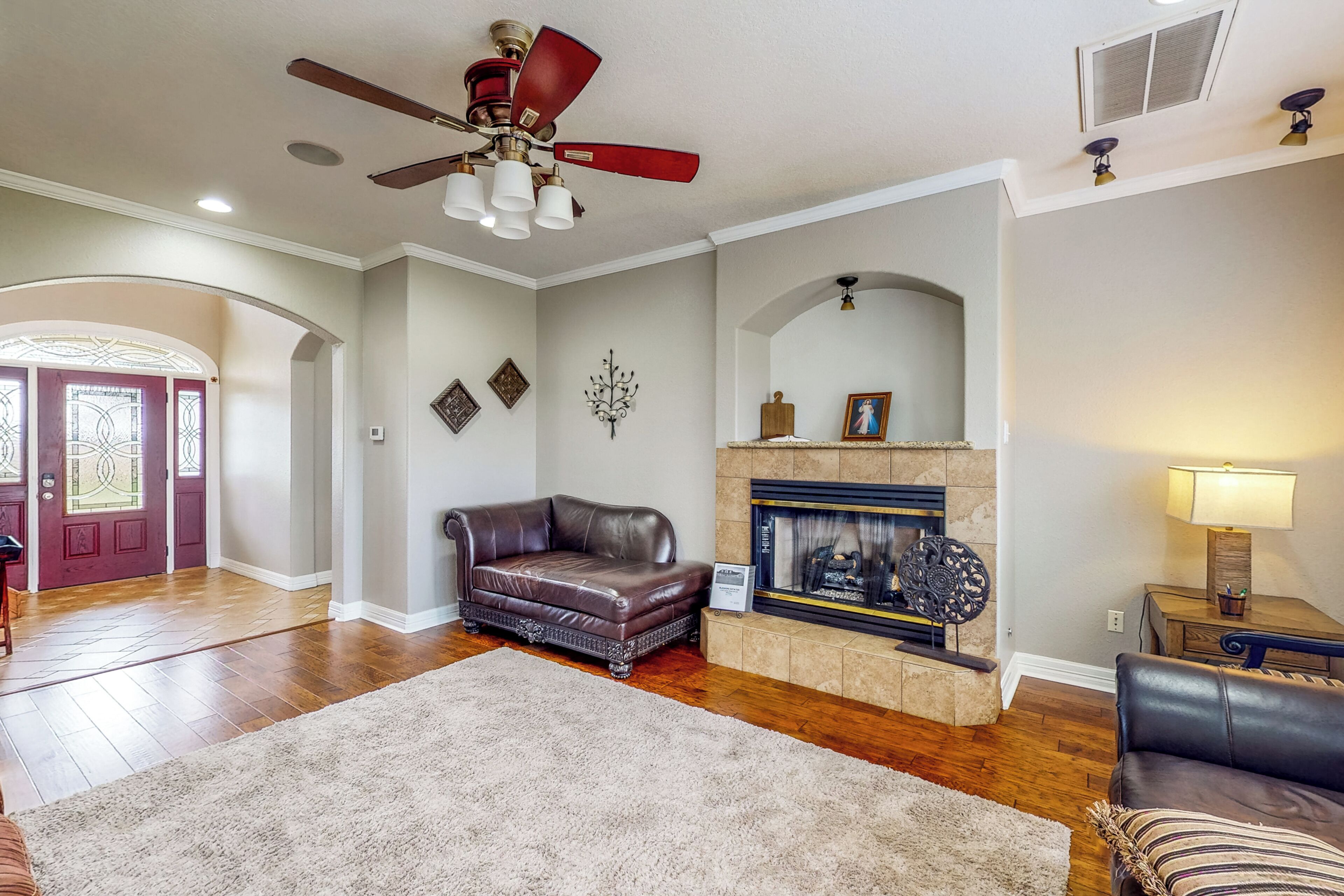 A living room with hardwood floors, a leather sofa, a fireplace, and a ceiling fan.
