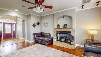 A living room with hardwood floors, a leather sofa, a fireplace, and a ceiling fan.