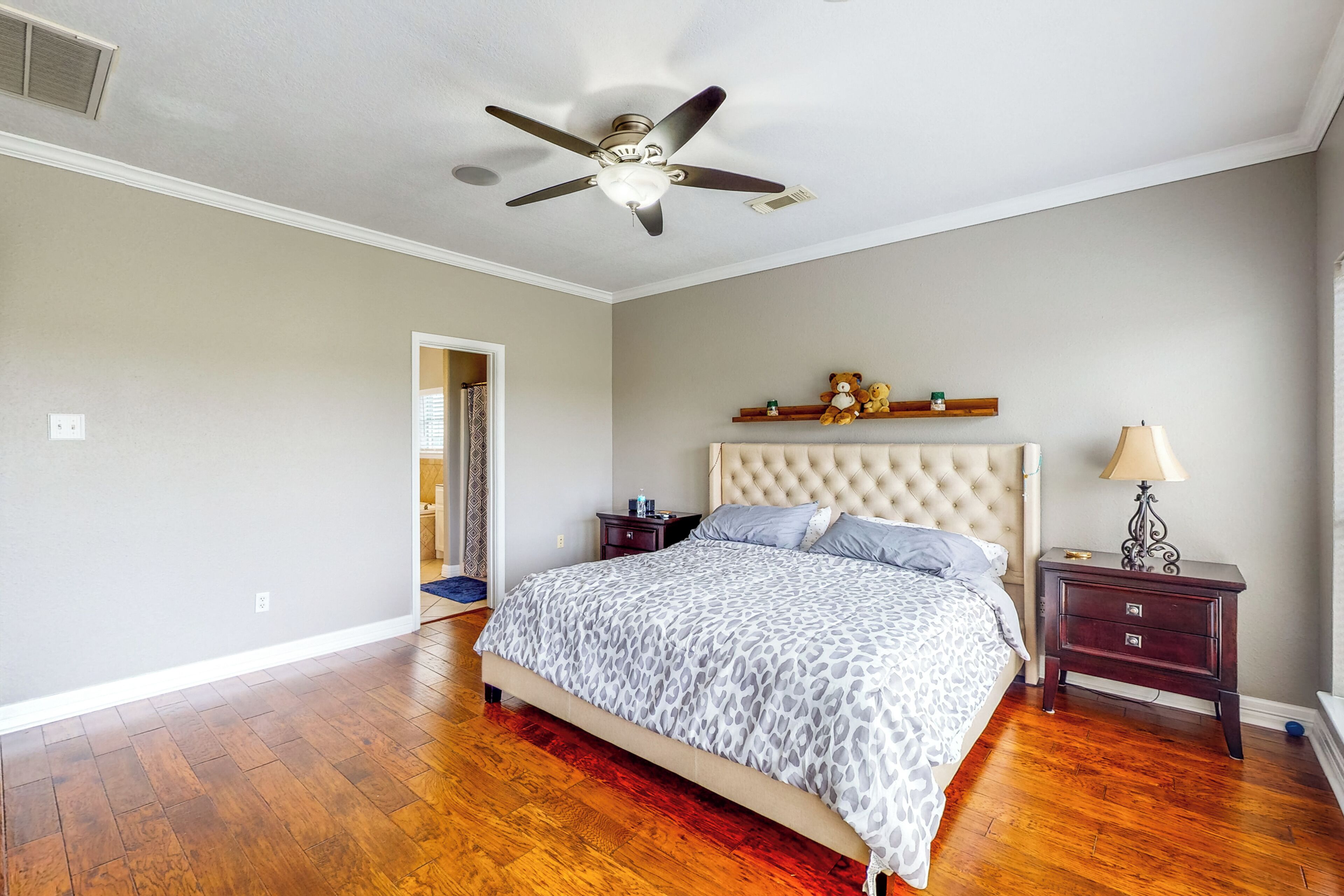 A bedroom with a tufted headboard, a bed with a leopard print bedspread, a nightstand with a lamp, and a ceiling fan.
