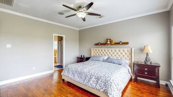 A bedroom with a tufted headboard, a bed with a leopard print bedspread, a nightstand with a lamp, and a ceiling fan.