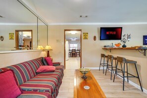 A living room with a sofa, a dining table, bar stools, a TV, and a mirror. - Hot Tub & Game Room! Home 15 Mi to At&t Stadium (North Richland Hills)