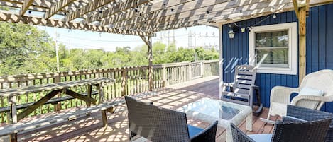 A covered outdoor deck with wooden benches, wicker chairs, and a glass table.