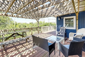 A covered outdoor deck with wooden benches, wicker chairs, and a glass table.