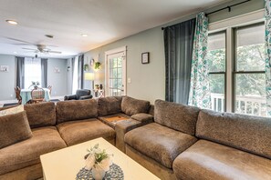 A living room with a sectional sofa, a dining table, a ceiling fan, and a window with curtains.
