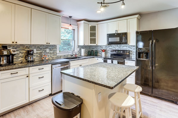 A modern kitchen with white cabinets, granite countertops, stainless steel appliances, and a large island with bar stools.