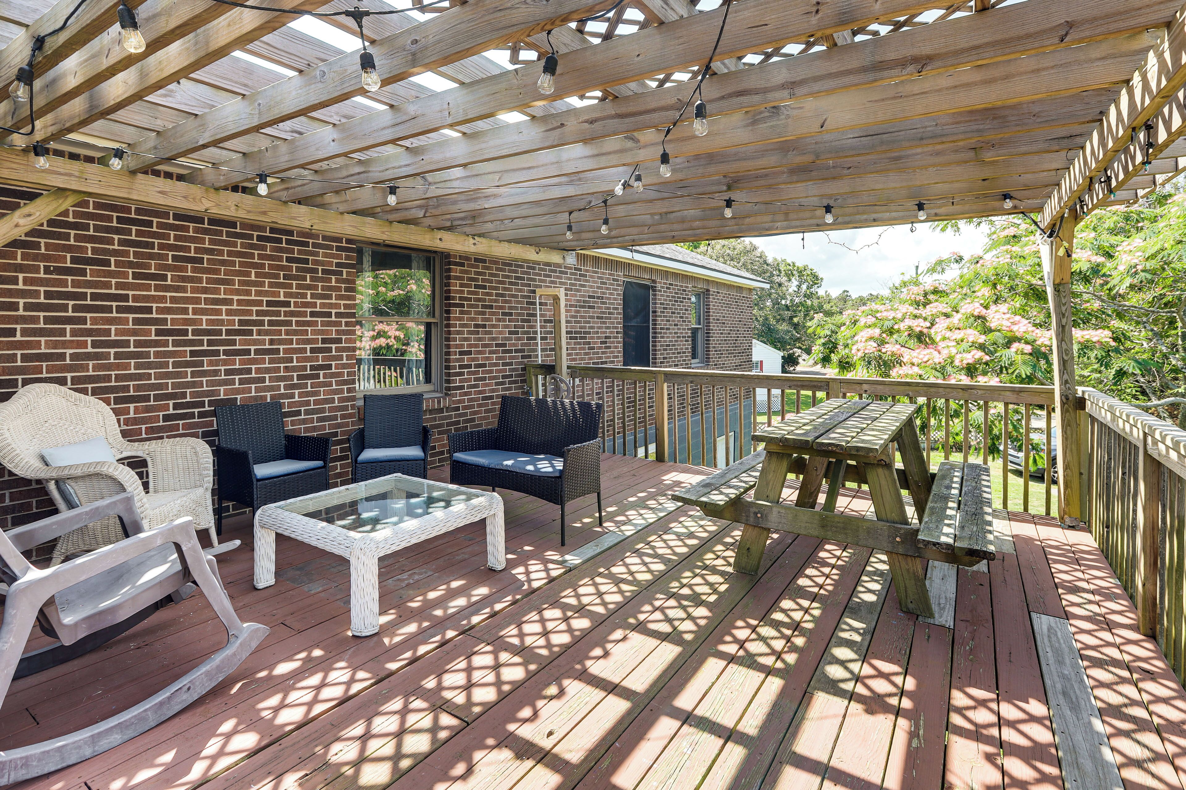 A covered patio with wooden flooring, outdoor furniture, and a brick wall.