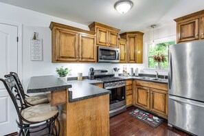 A kitchen with wooden cabinets, stainless steel appliances, a granite countertop, and a dining area with a chair. - Fire Pit & Steps to Lake! Tims Ford Lake Retreat (Lynchburg)