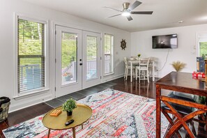 Un vaste salon doté d’un ventilateur de plafond, d’un téléviseur fixé au mur, d’un coin repas avec une table et des chaises, et de grandes portes-fenêtres coulissantes donnant sur un balcon.