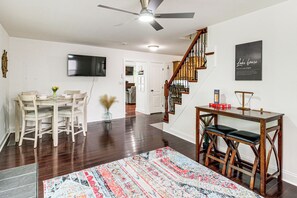 Un salon moderne comprenant un coin repas, un escalier et un téléviseur à écran plat fixé au mur.