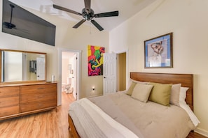 A bedroom with a bed, a ceiling fan, a dresser, a mirror, and two doors.