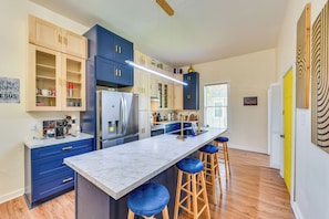 A modern kitchen with a marble countertop, wooden stools, and a variety of cabinets.