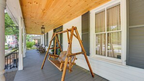A wooden swing set on a porch with a white railing and a window with shutters.