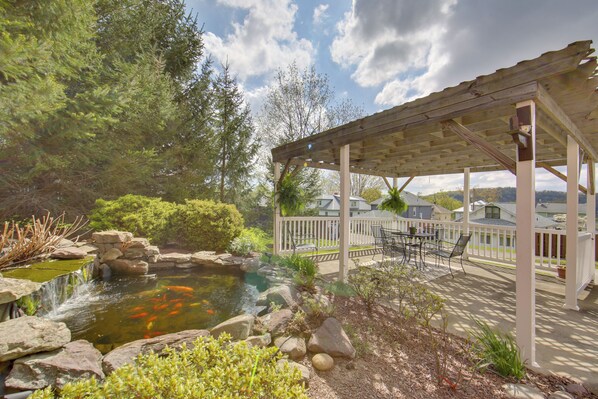 A covered patio with outdoor furniture, a pond with fish, and a view of houses in the background. - Work, Play & Explore: 9-unit New Kensington Base (New Kensington)