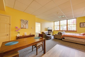 A room with a wooden dining table, a sofa, a bed, and large windows. - Work, Play & Explore: 9-unit New Kensington Base (New Kensington)