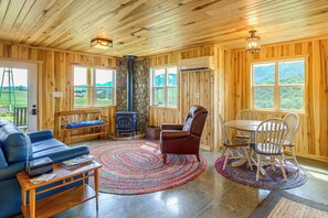 Un interior de madera con un sofá, una chimenea, una mesa de comedor con sillas y ventanas amplias.