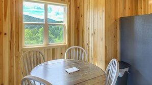 A wooden-paneled room with a round table, two chairs, a window with a view of greenery, and a refrigerator. - Pet-friendly Home w/ Stunning Views in Sparta! (Sparta)