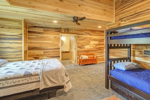 Quarto estilo cabana de madeira com beliches, ventilador de teto e um pequeno banco de madeira.