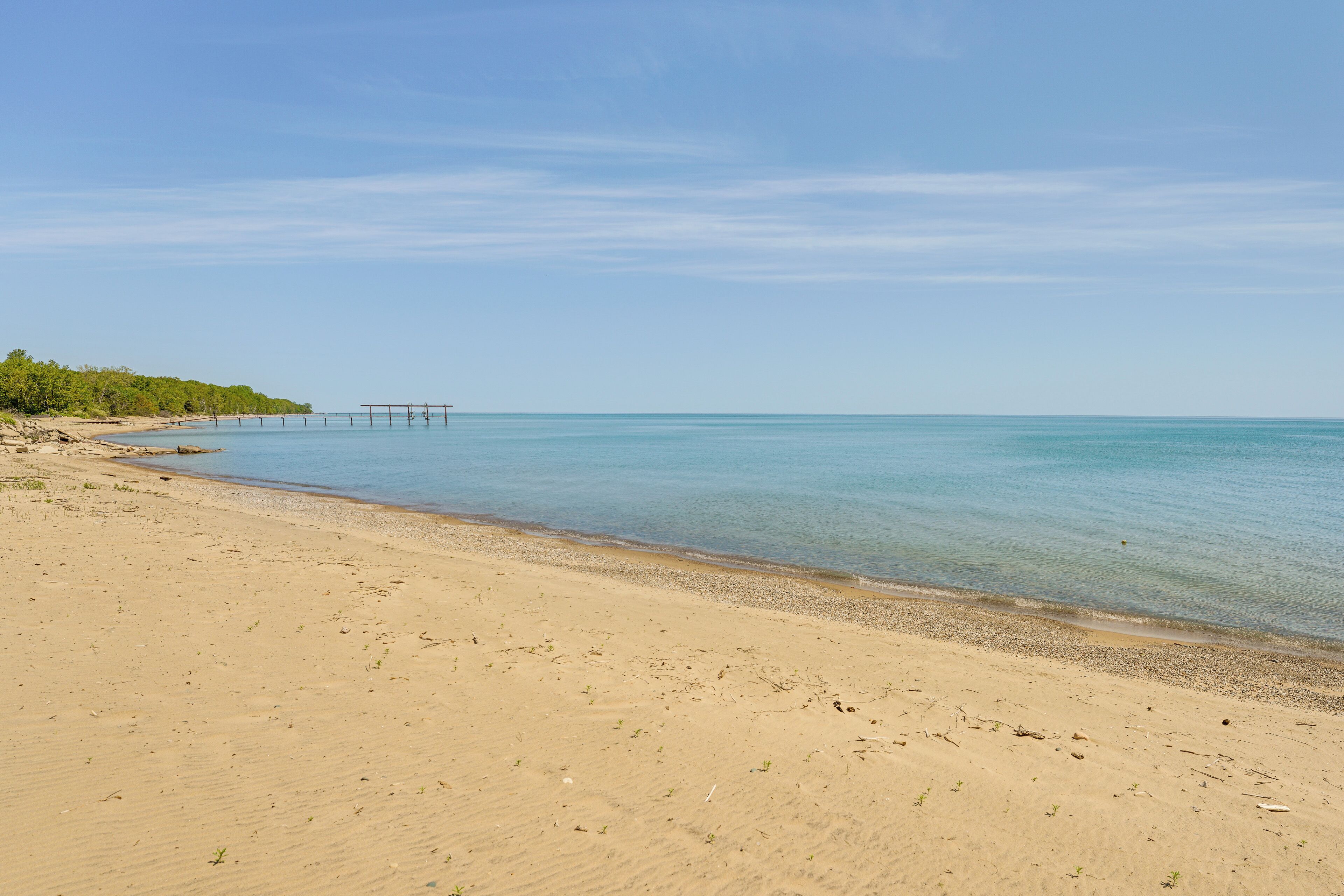 A beach with clear water, a pier, and a distant shoreline with greenery.