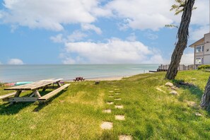 Uma área gramada com uma mesa de piquenique e um banco, um deck de madeira e vista para o oceano.