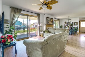 Uma sala de estar ampla com um sofá grande, um ventilador de teto e vista pela porta de vidro.