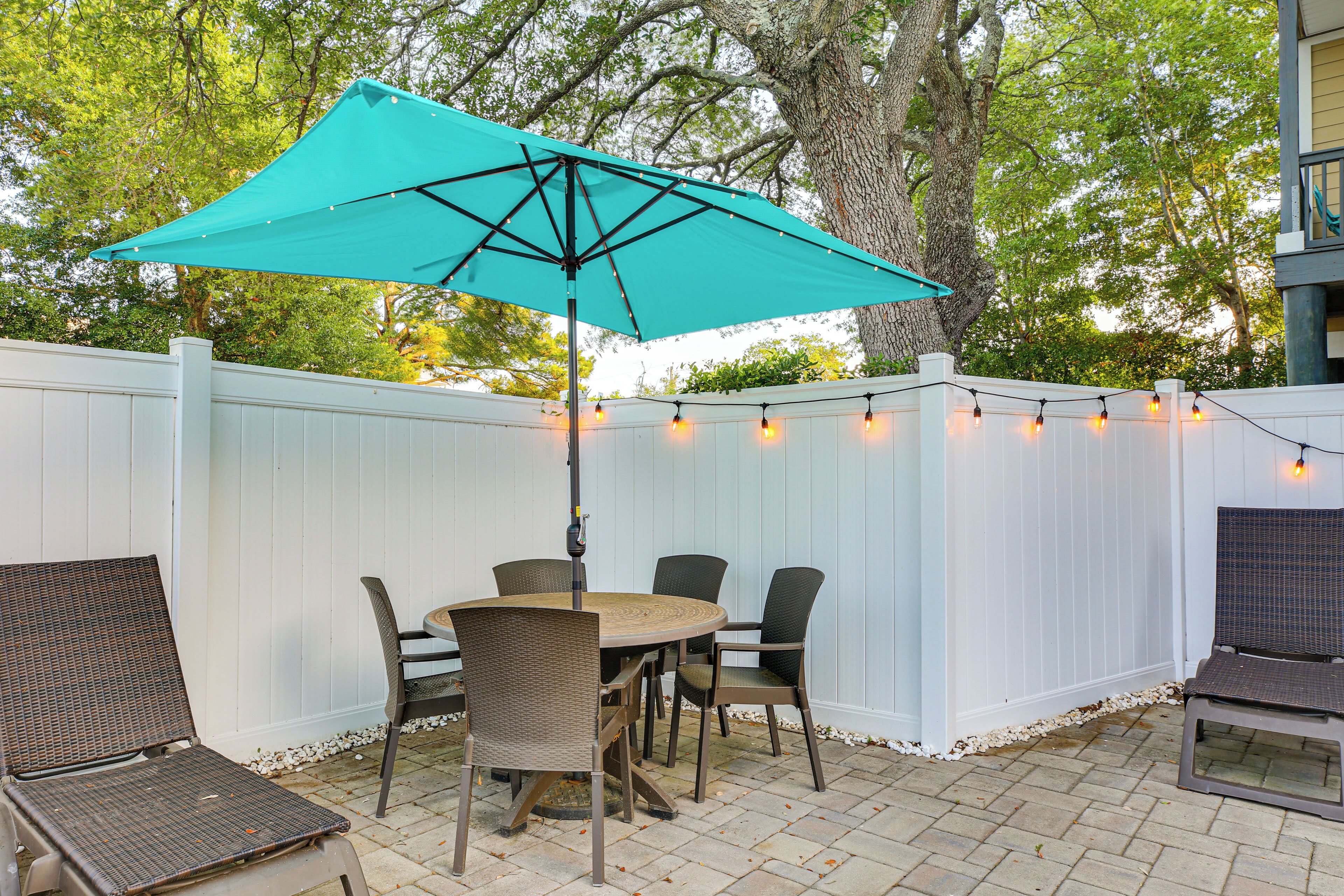 A patio with a table and chairs, a turquoise umbrella, and string lights.
