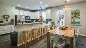 A kitchen with white cabinets, a wooden island with stools, a chandelier, and a painting of a palm tree. - Shared Pool & Hot Tub! Seaside Murrells Inlet Home (Murrells Inlet)