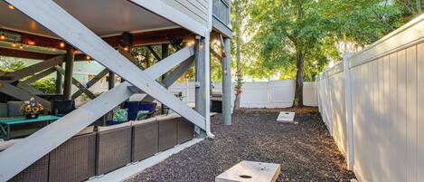 A covered outdoor area with a wooden playhouse, a covered seating area with furniture, and a white fence.