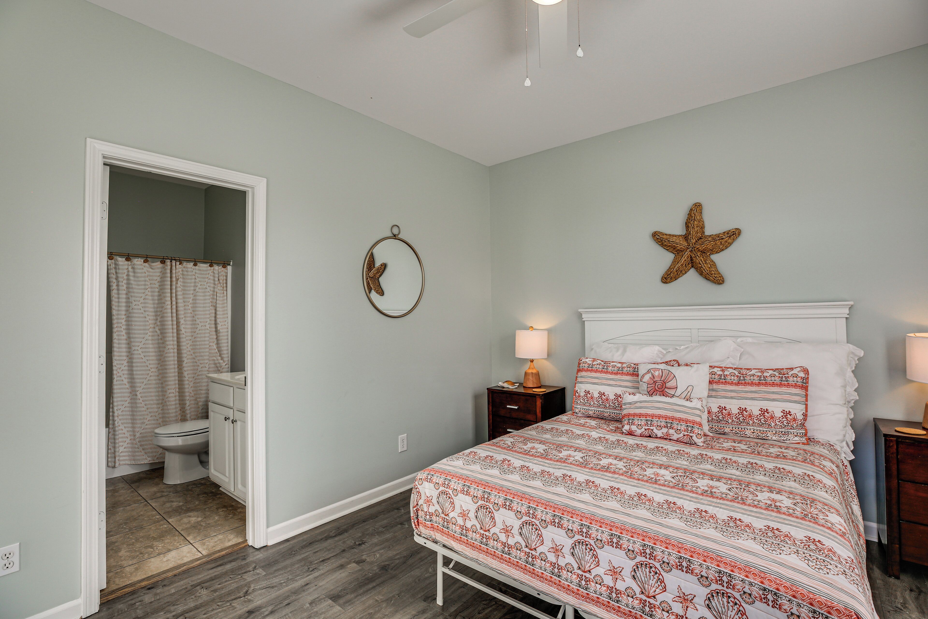 Una camera da letto con un letto, un comodino, una decorazione a forma di stella appesa al muro, una porta che dà su un bagno e una ventola a soffitto.