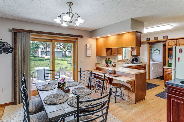 A kitchen with a dining area, wooden cabinets, a refrigerator, and a large window.