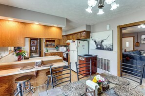A kitchen with wooden cabinets, a refrigerator, bar stools, and a dining table.