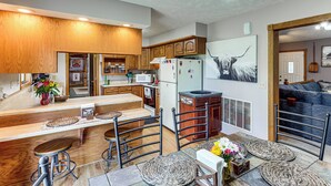 A modern kitchen with wooden cabinets, a central island with stools, and a dining area with a sofa and a painting.