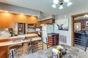 A modern kitchen with wooden cabinets, a central island with stools, and a dining area with a sofa and a painting.