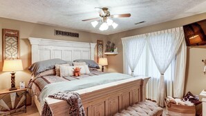 A bedroom with a wooden bed, a bench, a ceiling fan, and a 'FARMHOUSE' sign on the wall.