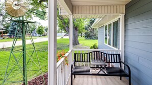A porch with a bench and a windmill, a house in the background, and a well-maintained lawn.