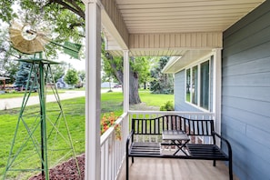 A porch with a bench and a windmill, a house in the background, and a well-maintained lawn.