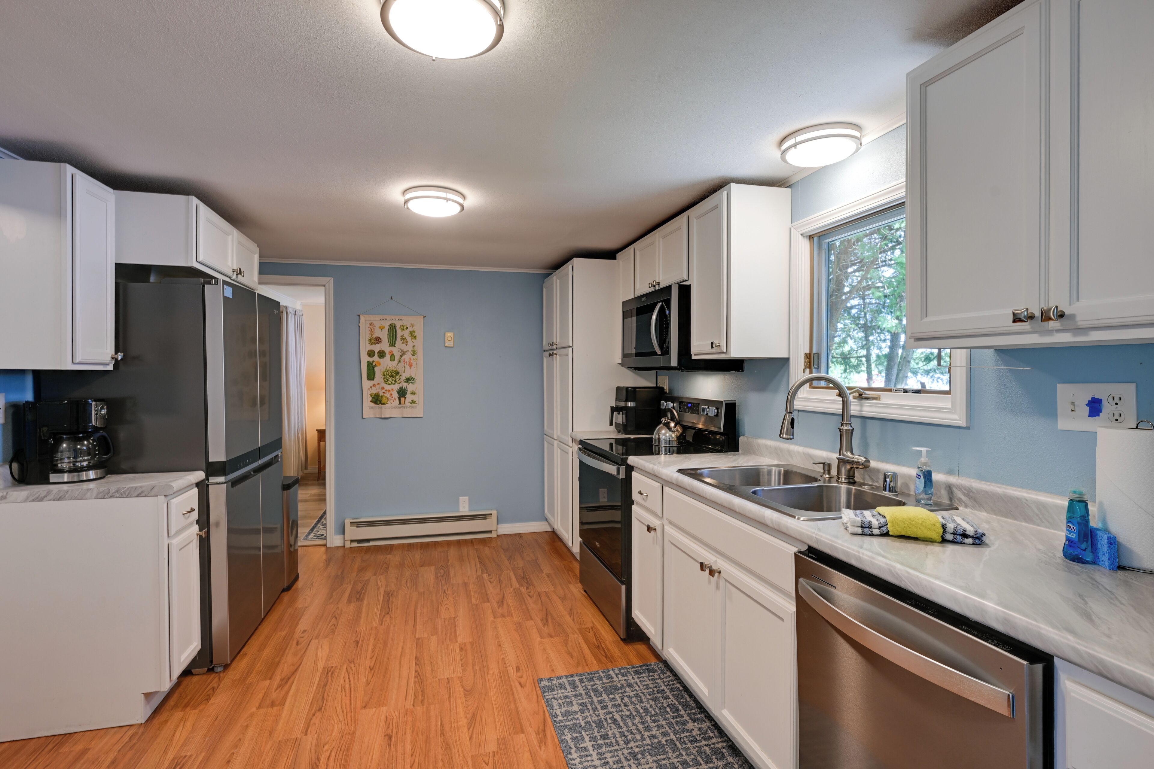 A kitchen with white cabinets, stainless steel appliances, a window, and a sink.