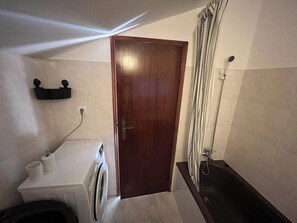 A compact bathroom with a washing machine, a shower, and a wooden door.