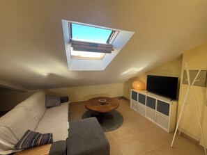 A living room with a sofa, a coffee table, a TV on a cabinet, and a skylight.