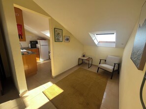 A small, well-lit room with a kitchenette, a sofa, a small table, and a window.