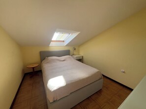 A bedroom with a bed, a bedside table, a nightstand, a small round table, and a skylight.