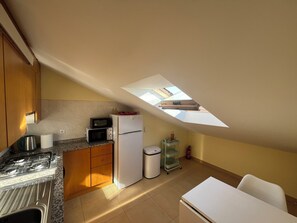 A kitchen with a skylight, a stove, a microwave, a refrigerator, and a trash bin.