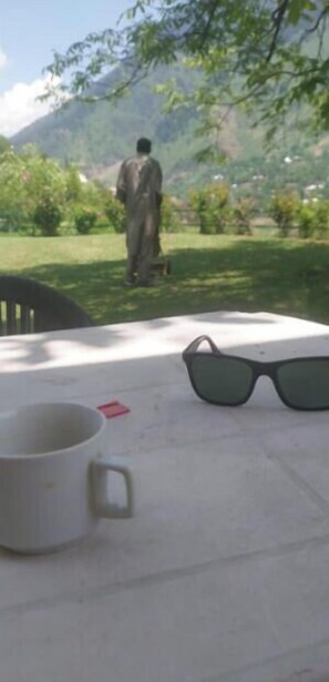 A table with a white mug, black sunglasses, and a person walking in a mountainous area. - Ahmed Lodge (Gund)