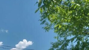 Área externa com gramado, mesa e cadeiras sob um guarda-sol colorido, cercada por vegetação e montanhas.